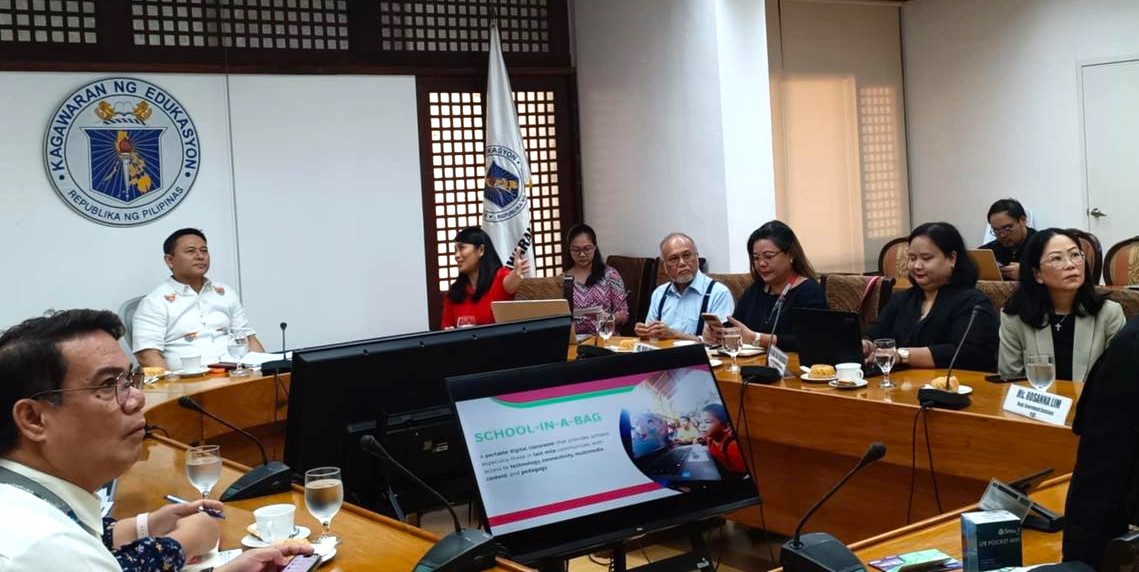 PLDT and Smart AVP and Head of Stakeholder Management Stephanie V. Orlino (seated, in red) explains to DepEd Secretary Sonny Angara the PLDT Group's flagship education program - School-in-a-Bag (SIAB)